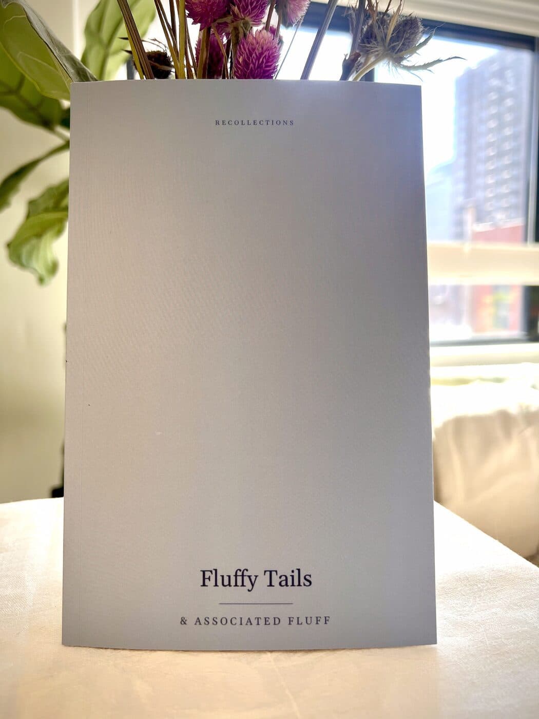 A pale blue softcover photo book titled Fluffy Tails standing on a table, its flexible cover bowing